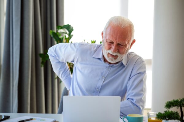 Senior businessman working sitting at desk suffers from lower back pain. Damage of intervertebral discs, spinal joints, compression of nerve roots caused by wrong posture and sedentary work